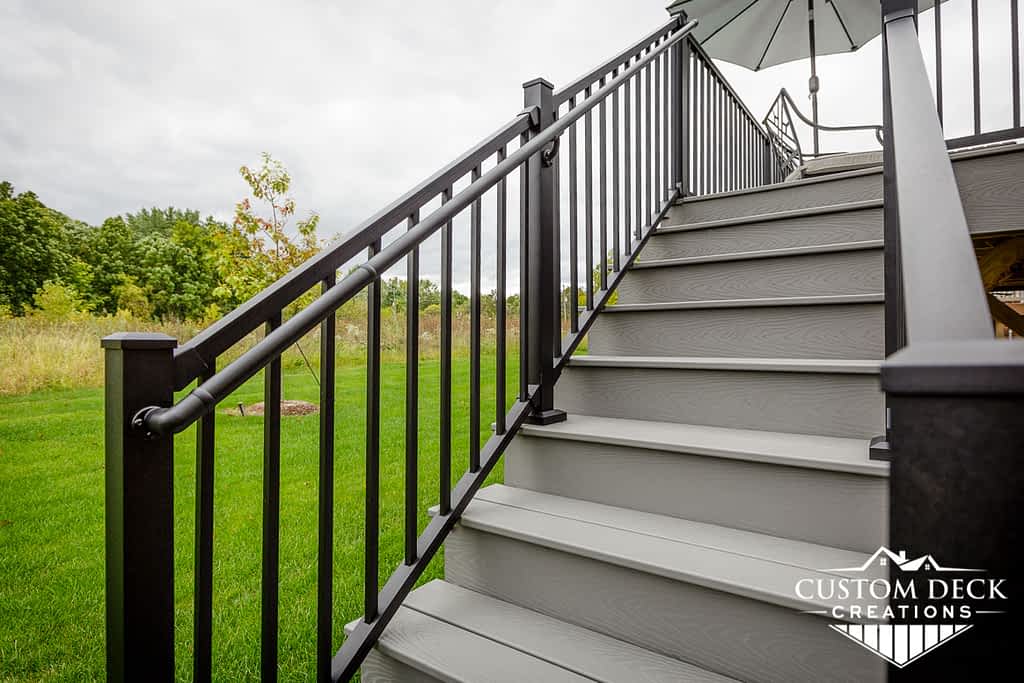 Grey stairs with black railing leading up to an exterior deck on the back of a condo