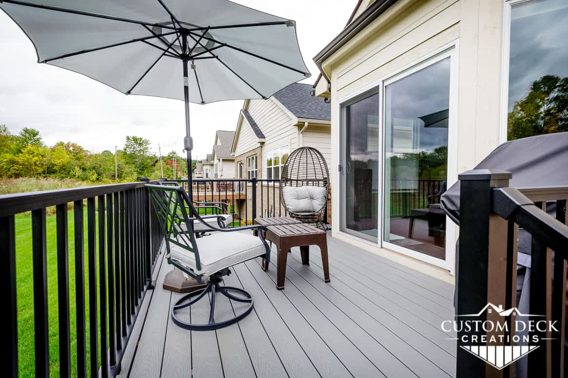 Grey backyard deck with black railing, shown with chairs, coffee table, and shade umbrella