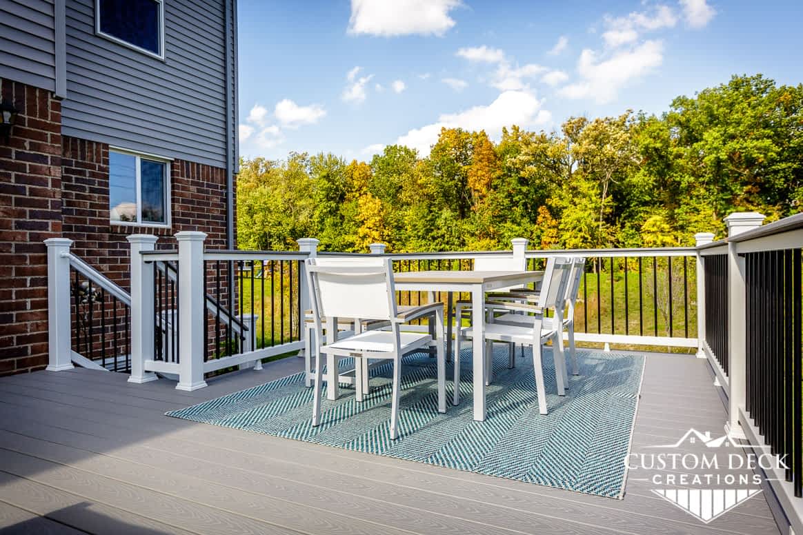 Grey backyard deck with seating area including table, chairs, and a bench