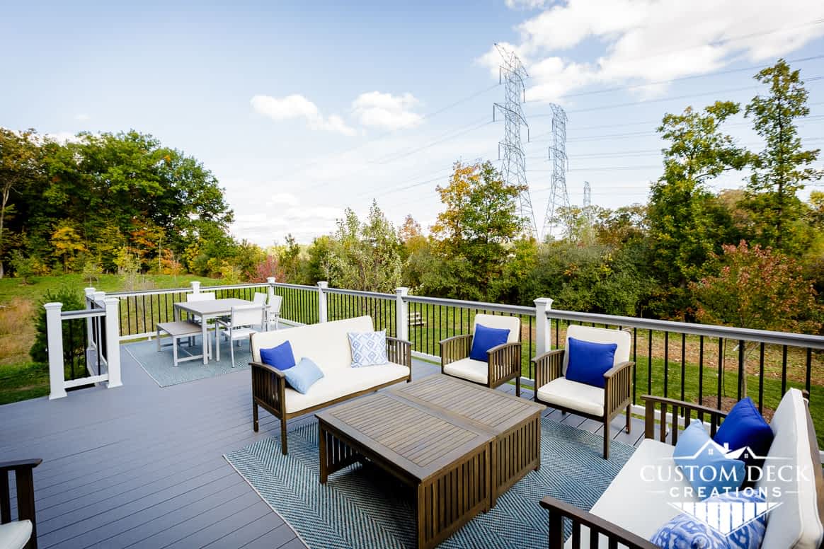 Grey deck with white railing, brown patio furniture, looking out to open space green backyard