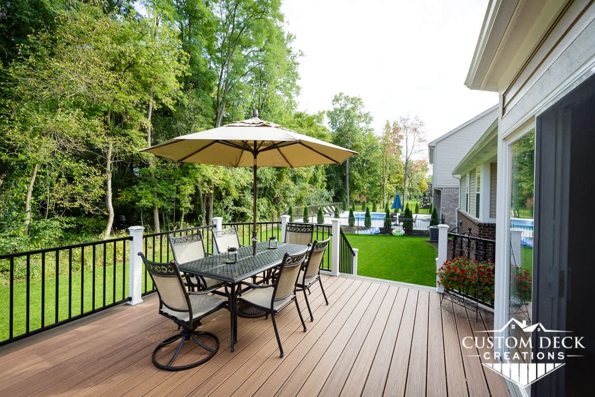 Brown exterior deck view in a neighborhood shown with white and black railings and shade umbrella