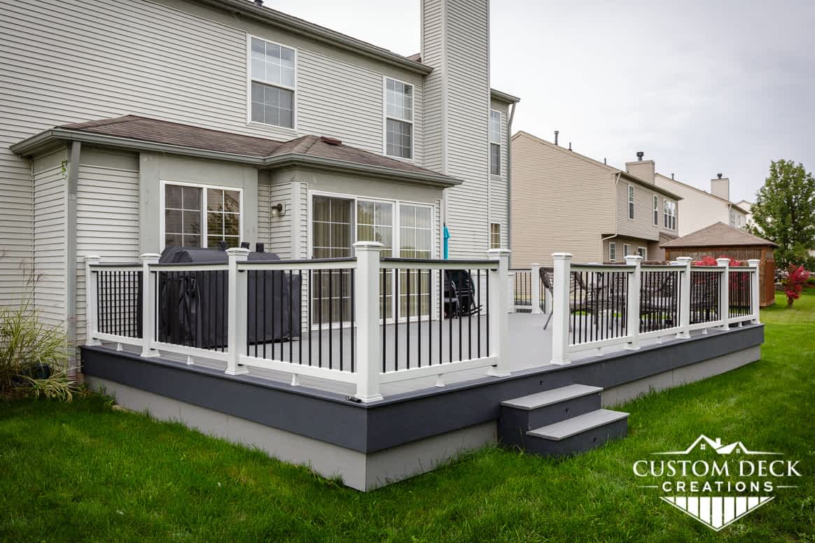 Deck on the back of a home with grey decking, white and black railing, and a grill