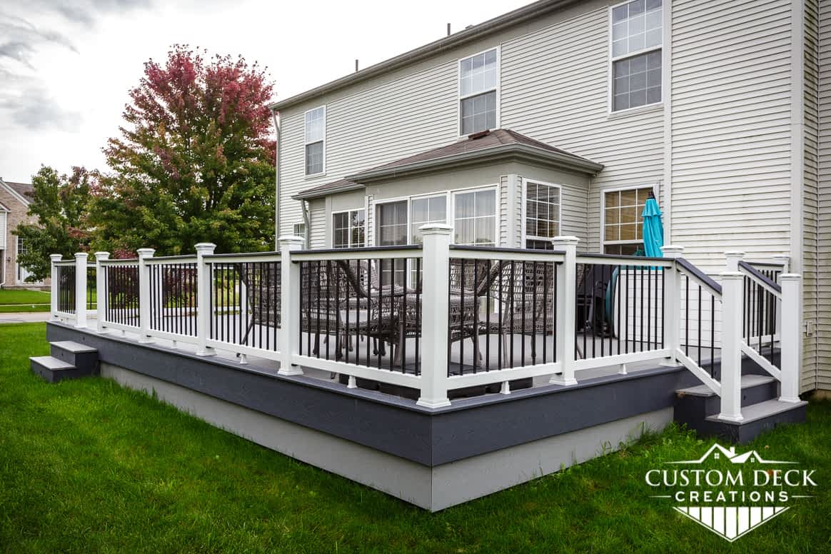 Grey outdoor deck in a backyard showing details of railing, two-tiered fascia, and stairs