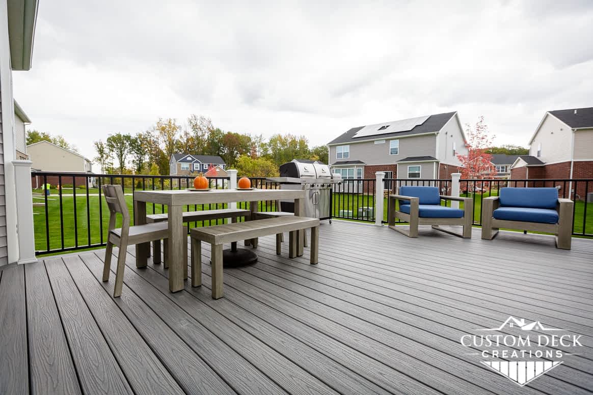 Grey deck with patio furniture and grill in the back of a new construction home