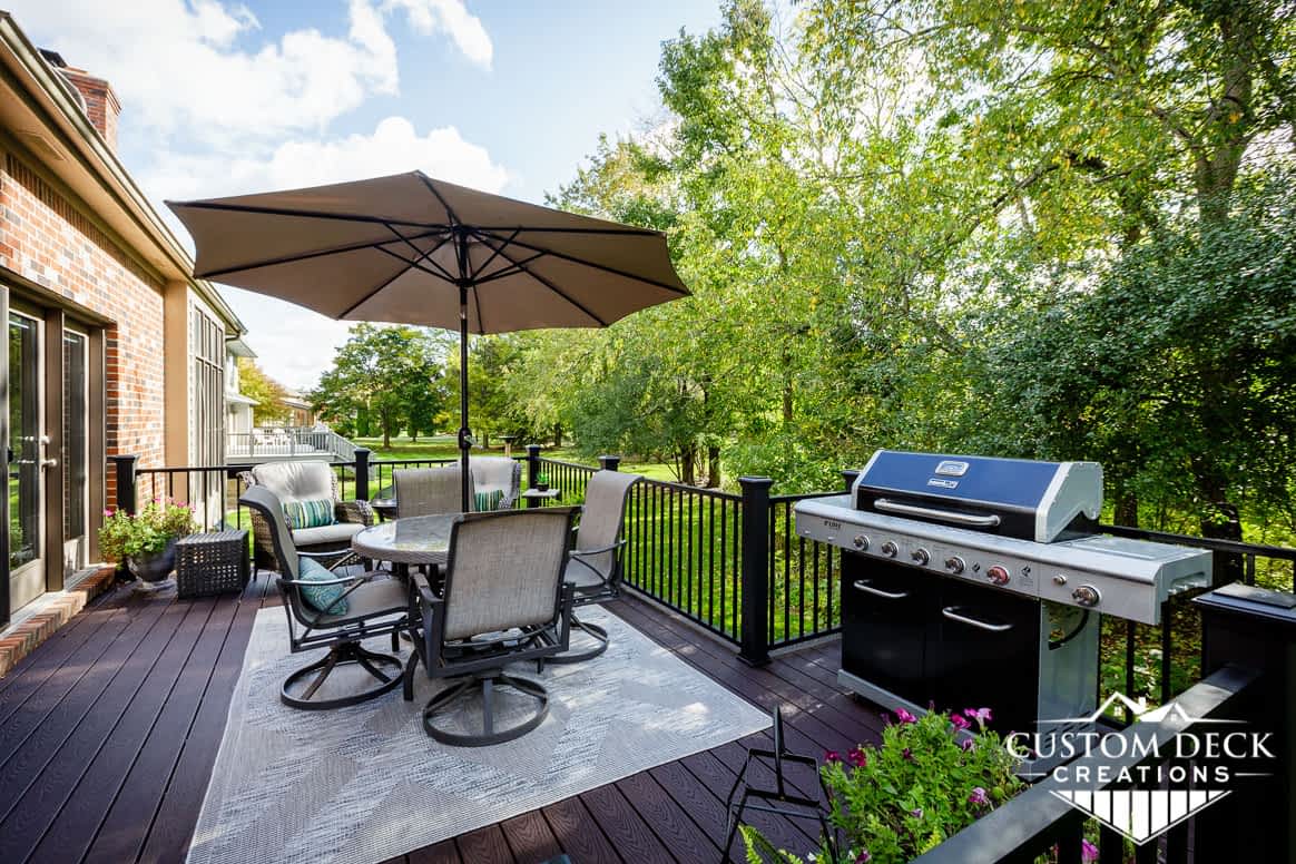 Grill, patio table, chairs, and umbrella on a brown backyard composite deck built by Custom Deck Creations