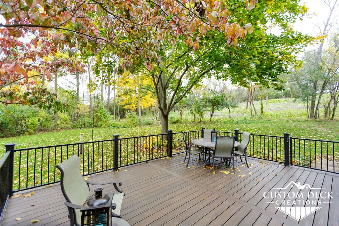 Brown backyard deck with a colorful Fall tree overhead and patio furniture