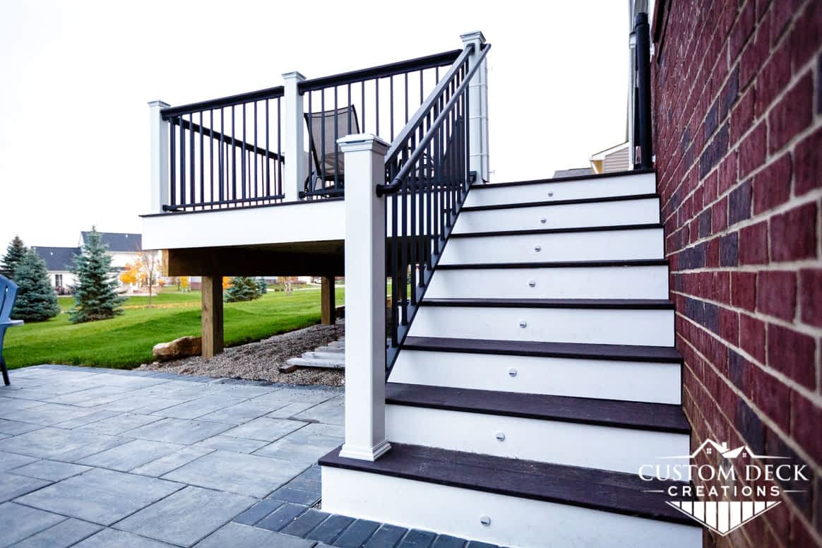 Stairs with small riser lights leading from a paver patio to a composite deck on the back of a home