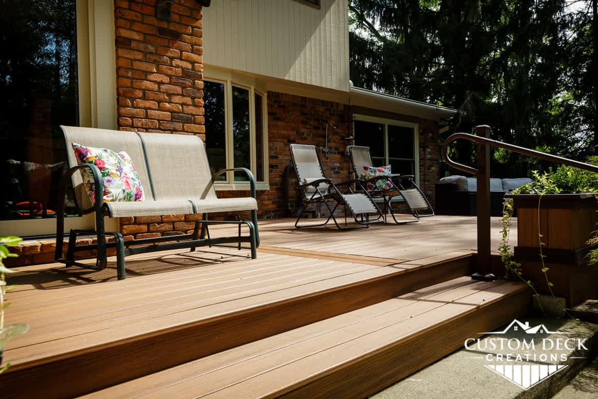 Steps of a ground level backyard deck shown with lounging patio chairs