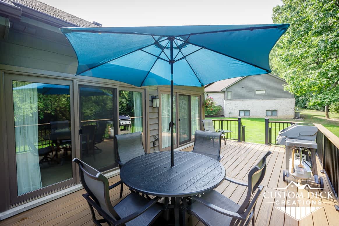 Backyard deck, brown decking, black and brown railing, and patio furniture with a shade umbrella