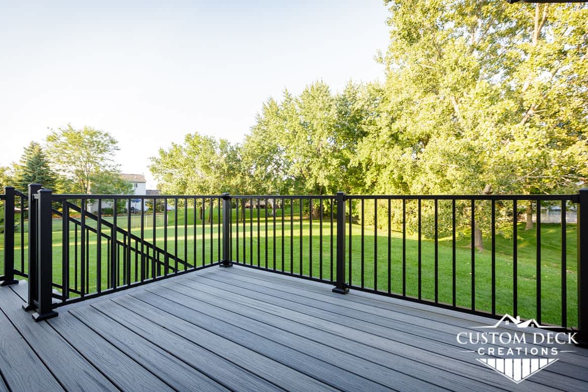 View of open green backyard on top of a grey and black composite backyard deck