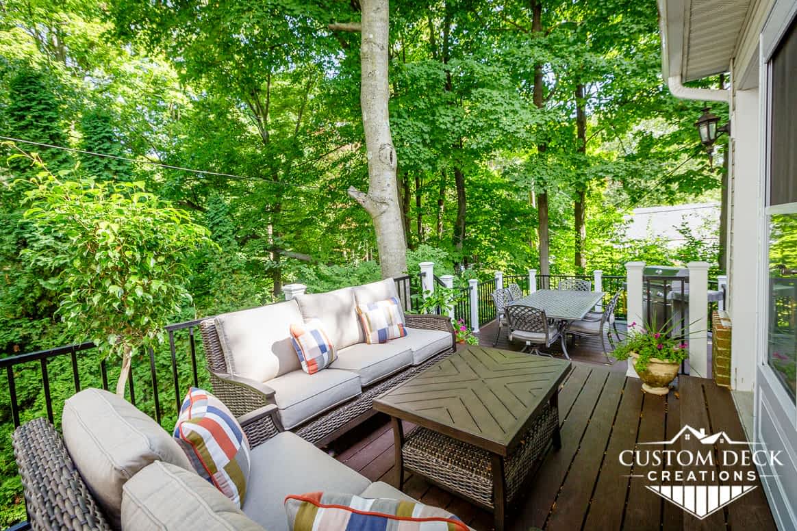 All brown deck with black and white railing in the middle of a forest with trees completely surrounding