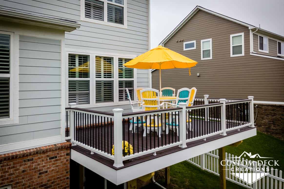 Aerial view of a brown, white, and black 2nd story backyard deck with colorful patio furniture and shade umbrella