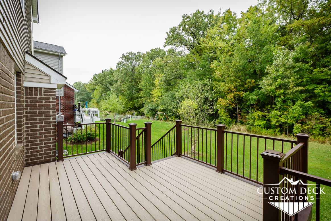 Taupe and brown backyard deck with brown and black railing, looking out to a beautiful green backyard view of a forest