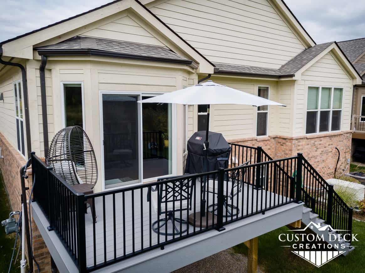 2nd story grey composite deck with black aluminum railing and stairs leading to backyard