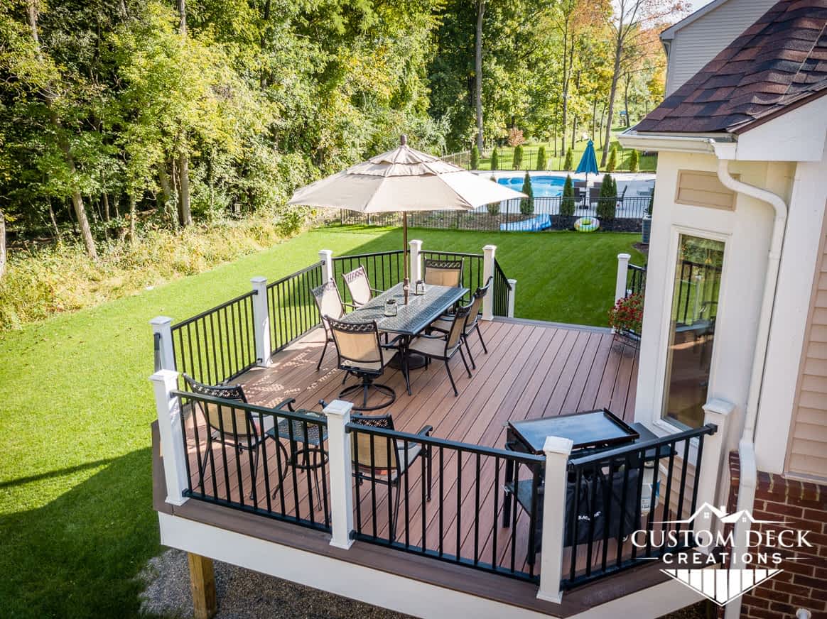 Two toned brown and white backyard deck with patio furniture, umbrella, and grill