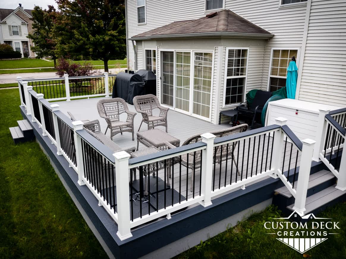 Two toned composite deck on the back of a home, shown with white and black railing