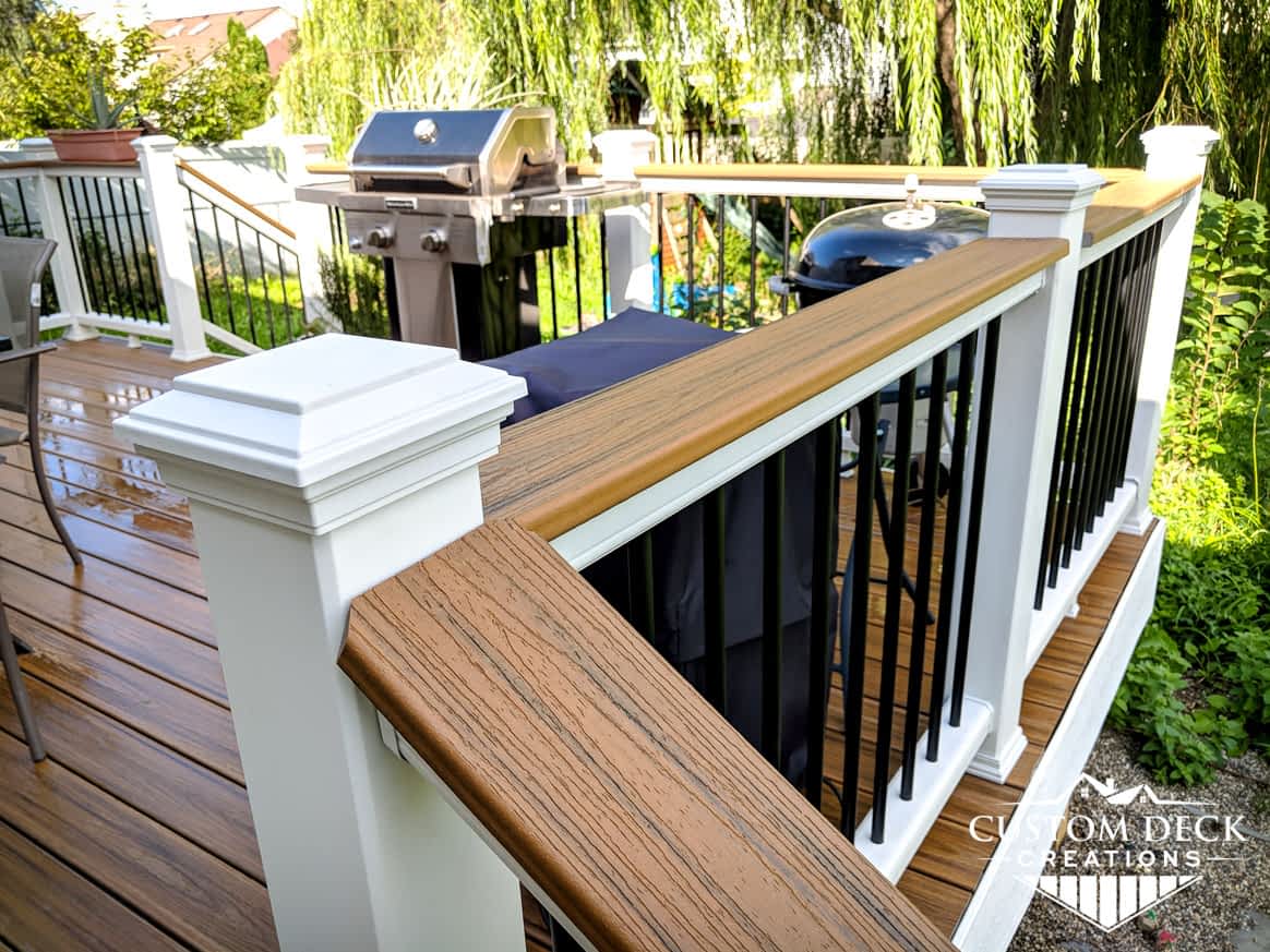 Drink rail decking board on top of white and black railing of a brown backyard composite deck
