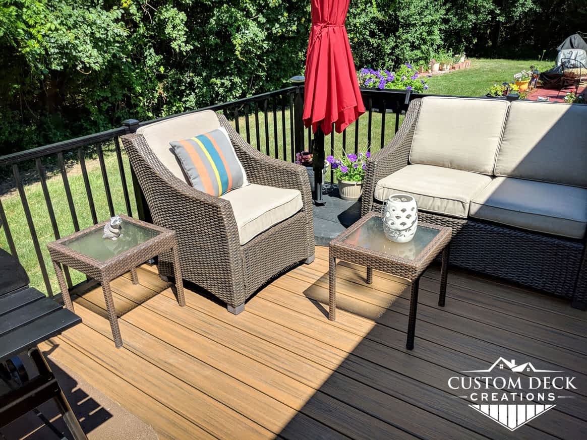 Patio furniture on a deck in a backyard with a red shade umbrella