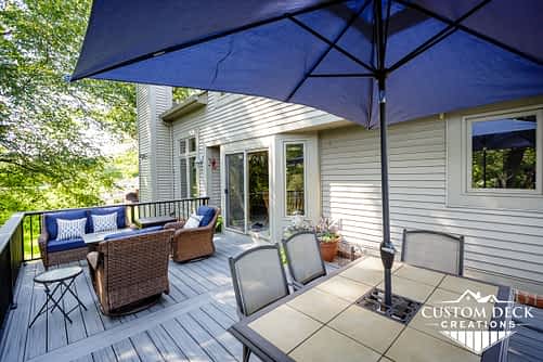 Shade umbrella and patio furniture on a grey outdoor 2nd story deck surrounded by tall trees