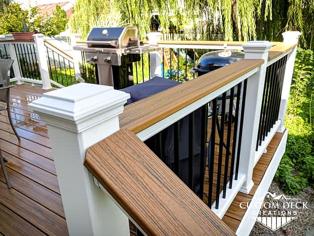 Drink rail decking board on top of white and black railing of a brown backyard composite deck